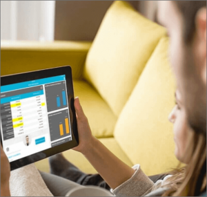 A woman sitting on a couch looking at a graph on a tablet with a man in the foreground looking over her shoulder.
